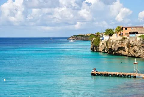 A serene ocean view with a dock and apartments perched on the coastline, creating a picturesque coastal scene.