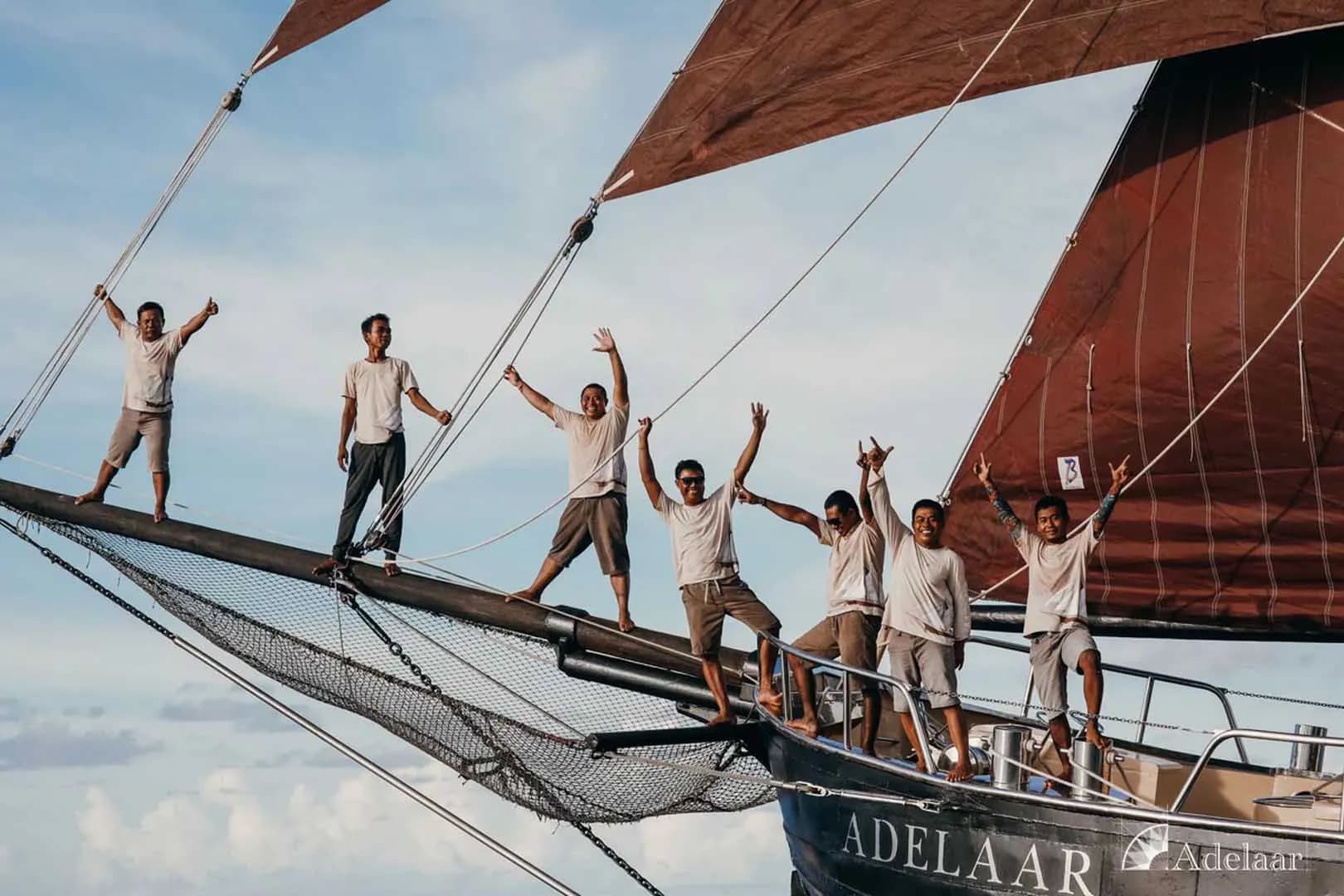 The Adelaar crew, a group of men on a sailboat, enthusiastically raising their arms in the air.
