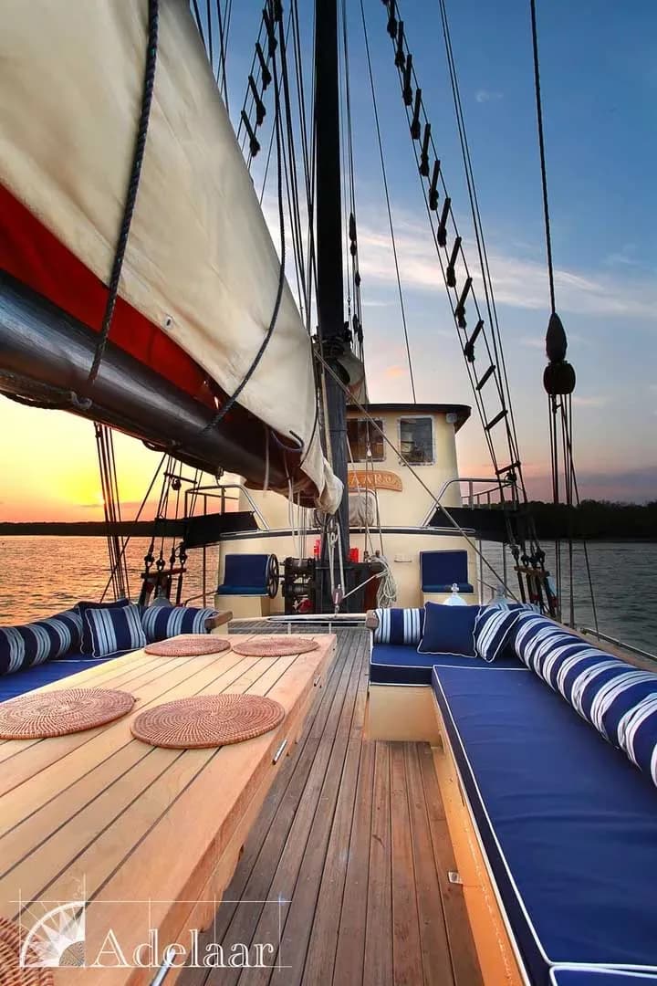 Deck of the Adelaar sailboat, featuring wooden planks and rigging, with a clear blue sky in the background.