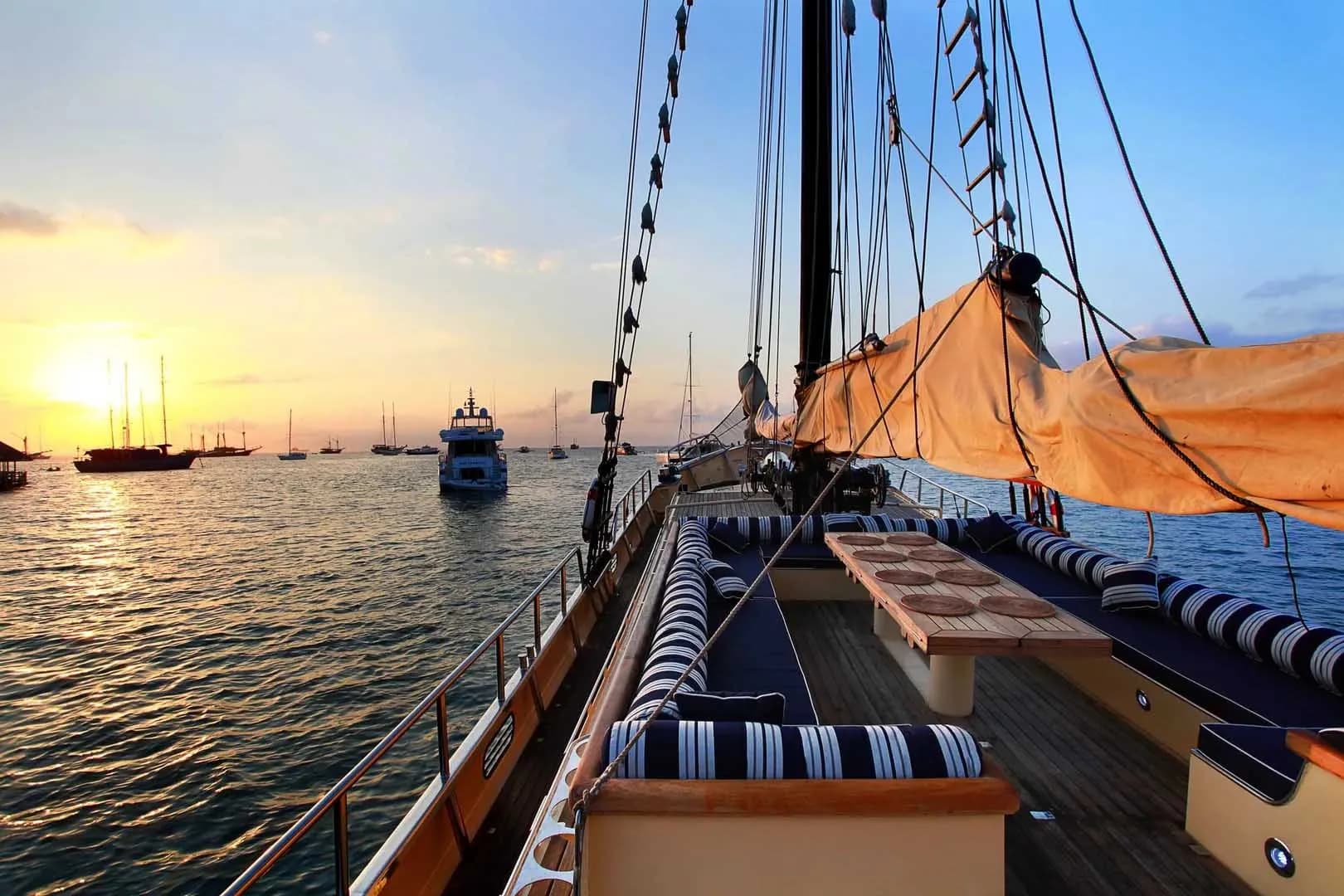 A sailboat named Adelaar is docked at sunset, casting reflections on the calm ocean waters.