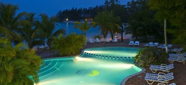 A swimming pool lit up at night at Fantasy Island Roatan Resort.