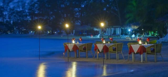 Tables set up for beachside dining at night at Fantasy Island Roatan Resort.