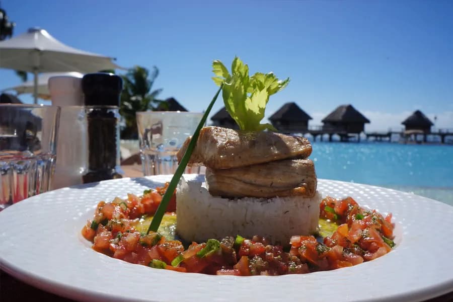 A plate with grilled fish on rice surrounded by a tomato salsa on a table next to the sea atManava Beach Resort & Spa Moorea A plate with grilled fish on rice surrounded by a tomato salsa on a table next to the sea atManava Beach Resort & Spa Moorea