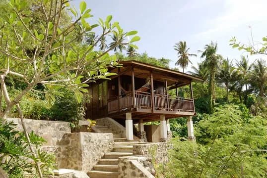 A bungalow is perched on a hillside surrounded by foliage A bungalow is perched on a hillside surrounded by foliage