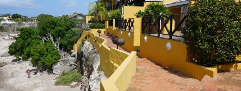 A sunny beachfront apartment with a yellow facade and a pathway leading to it.