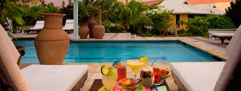 A selection of beverages on a table between two lounge chairs next to a swimming pool