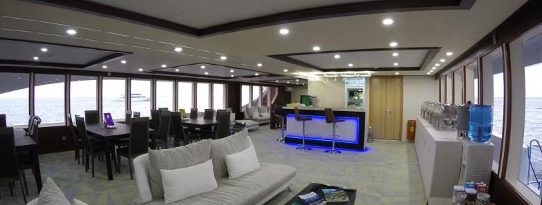 Inside the MV Emperor Serenity Liveaboard in the Maldives, a generously-sized lounge furnished with cozy couches and a television