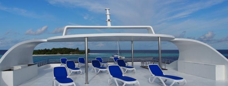 Deck of boat with lounge chairs under a clear blue sky. Enjoy the serene atmosphere on MV Emperor Serenity Liveaboard in the Maldives.