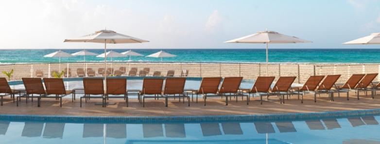 A swimming pool with a row of lounge chairs look onto the sea at Playacar Palace.