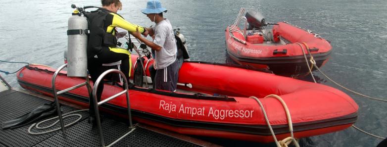 A scuba diver is helped onto a tender boat
