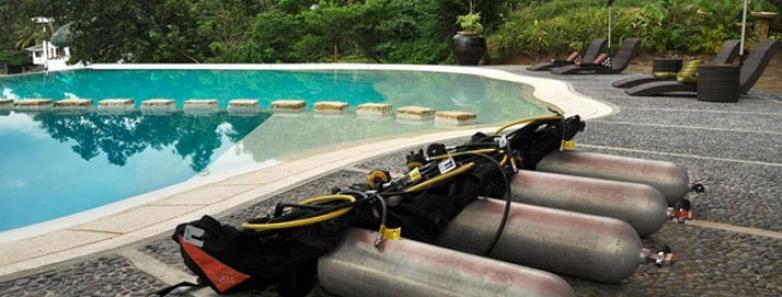 Four sets of scuba equipment lay next to the pool at Aiyanar Beach & Dive Resort