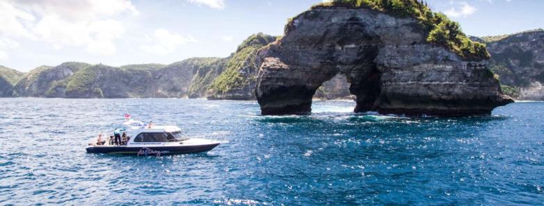 A small island with an arch and All 4 Diving's boat in Nusa Penida, Bali.