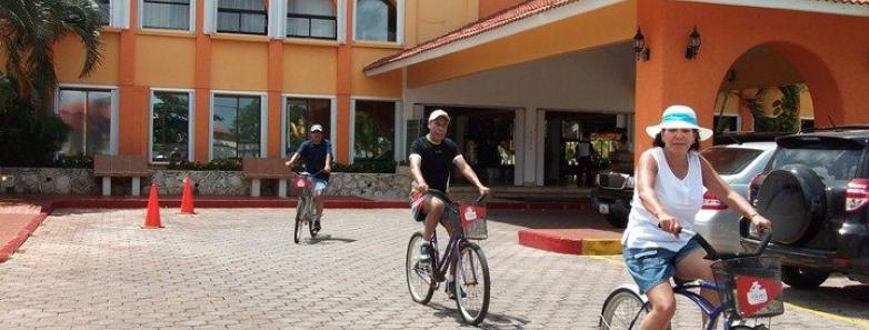 People riding bikes in front of a hotel. Enjoying a sunny day, they pedal along the street, creating a lively atmosphere.