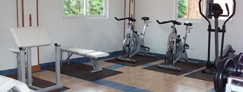 A well-equipped gym room with various exercise equipment and a large window providing natural light.