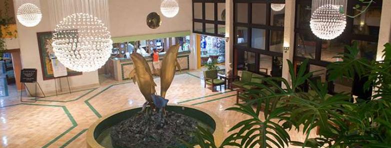 A grand lobby at Cozumel Palace hotel in Mexico, featuring a beautiful fountain and lush green plants.