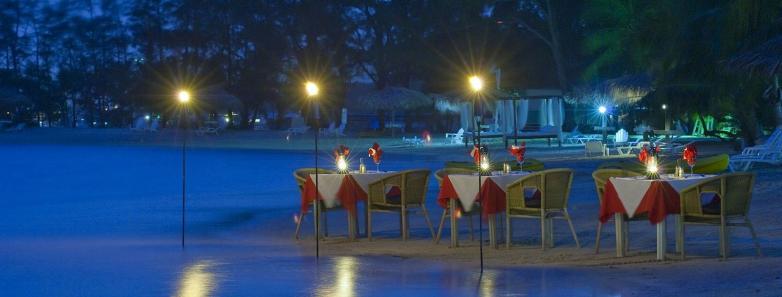 Tables set up for beachside dining at night at Fantasy Island Roatan Resort.