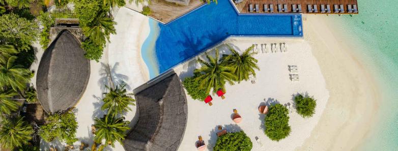 An aerial view of Kuramathi Island Resort with palm trees, a sparkling pool, and people enjoying the sun and sand.