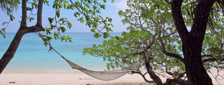 A hammock on a white sand beach with the sea in the background