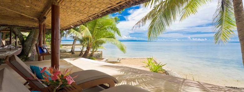 An oceanfront bure with beach beds looks onto a white sand beach at Toberua Island Resort Fiji.