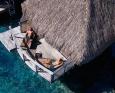 People lay on lounge chairs on an over-water deck at Manava Beach Resort & Spa Moorea